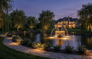 Alt: Elegant estate with illuminated pond and fountain at dusk