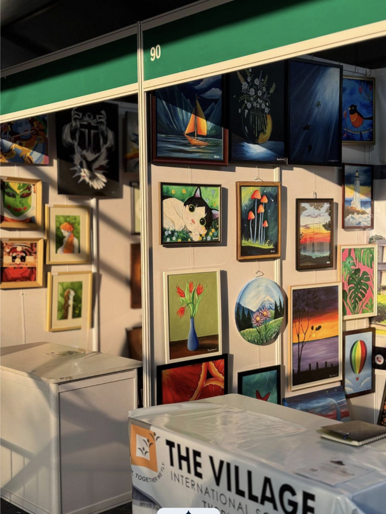 Art fair booth displaying framed paintings of animals, flowers, and landscapes. 