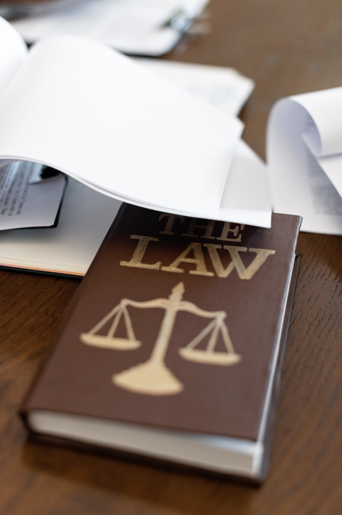 Law book with a scales-of-justice emblem on a desk covered in papers courtesy of Mikhail Nilov on Pexels