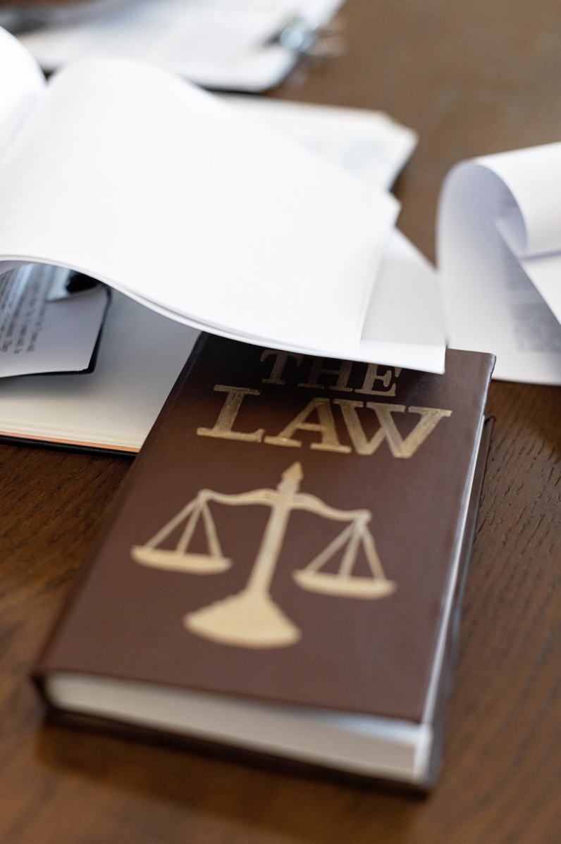 Law book with a scales-of-justice emblem on a desk covered in papers courtesy of Mikhail Nilov on Pexels